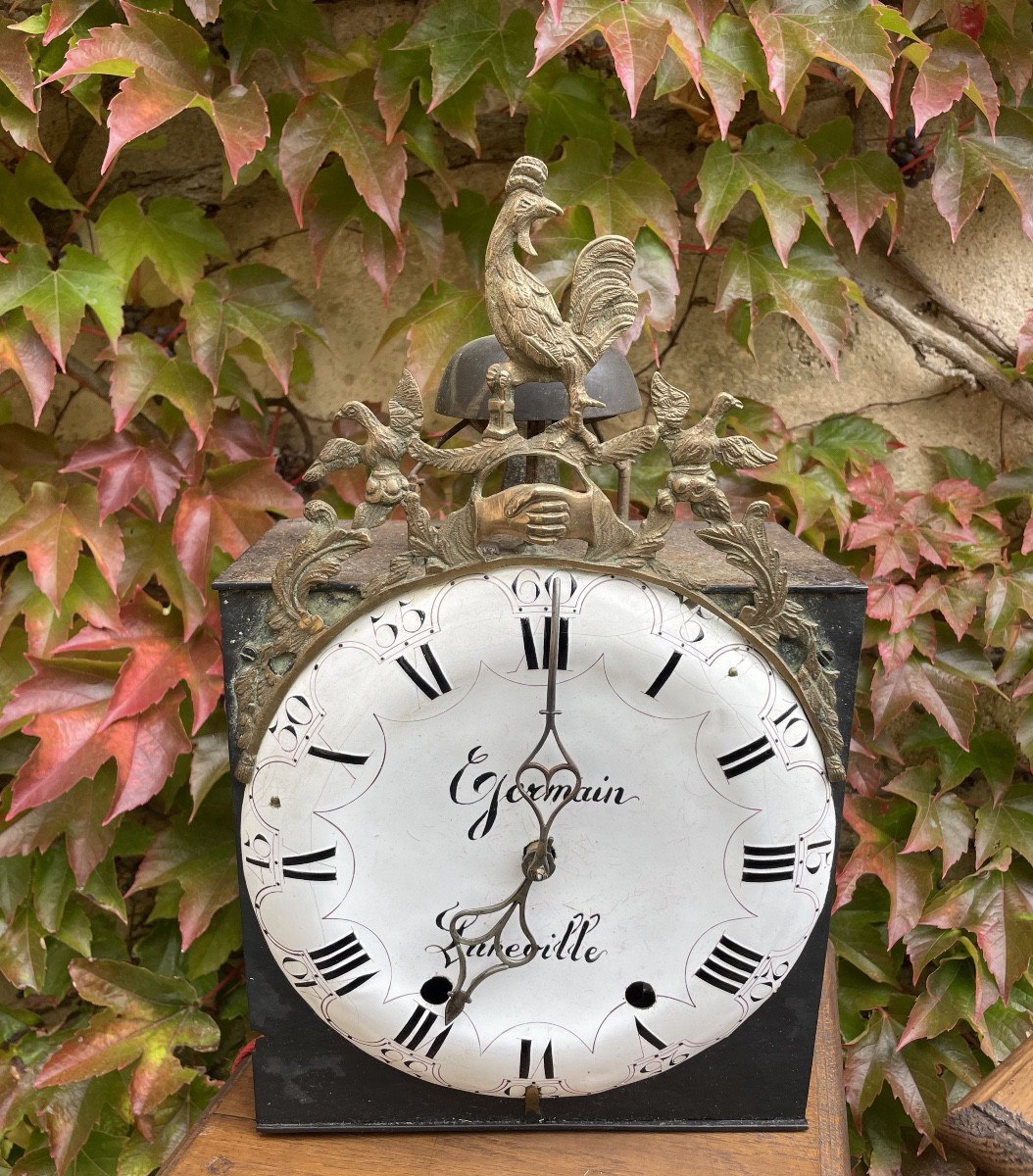 Front view of the 18th-century clock movement showing the enamel dial signed Germain Lunéville and cast brass rooster pediment