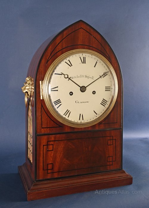 Three-quarter view of the lancet-top mahogany bracket clock showing dial, ebony inlay, and side lion-head mount