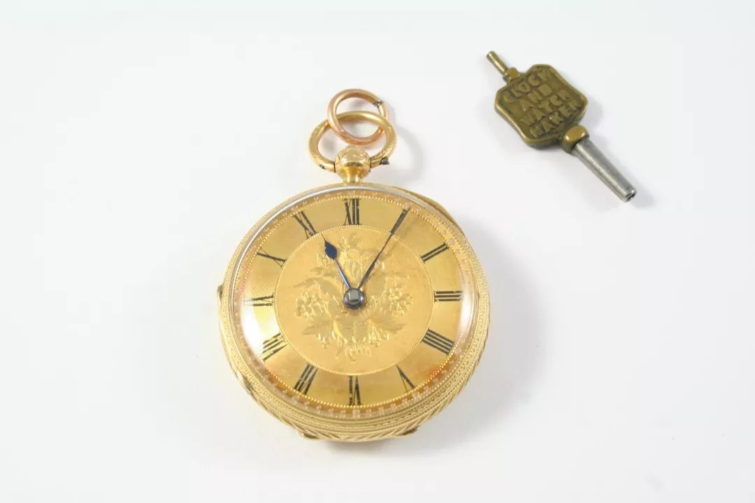 Front view of the 18ct gold open-faced pocket watch with foliate dial and accompanying watch key