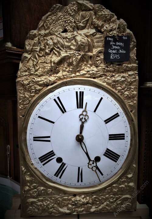 Front view of the Comtoise clock showing the embossed brass surround, dial, and trefoil hands