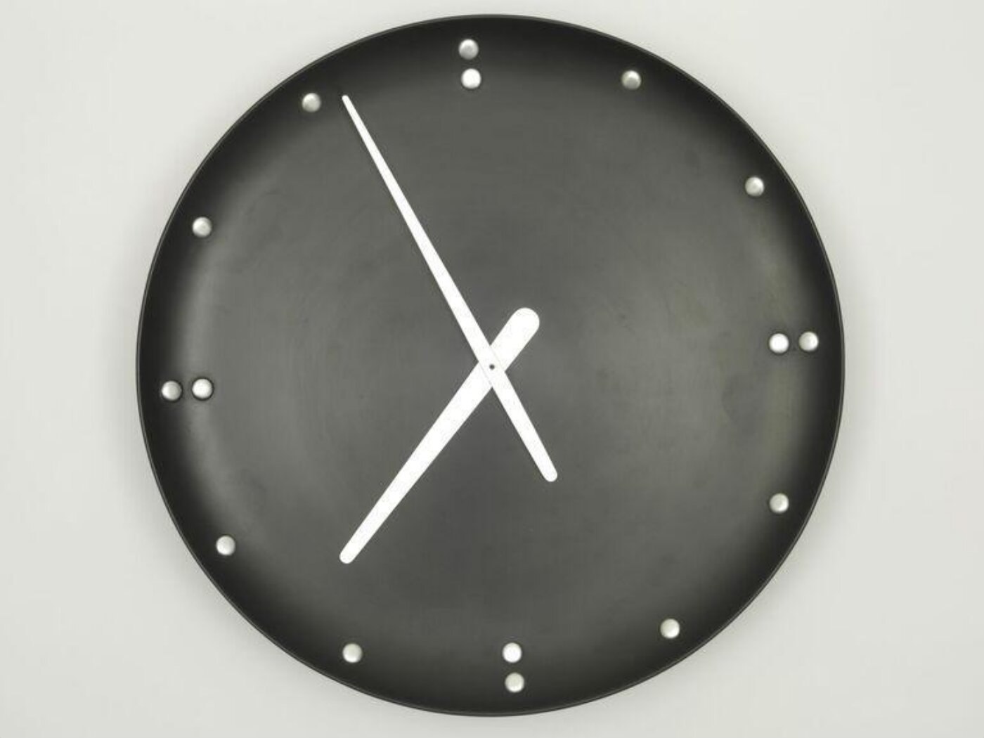 Front view of the circular wall clock showing the black dial, aluminium roundels, and aluminium hands.