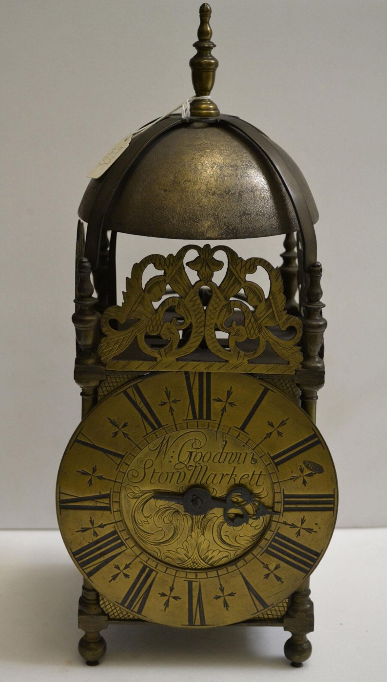 Front view of the brass lantern clock, showing the chapter ring, pierced cresting, and finials.
