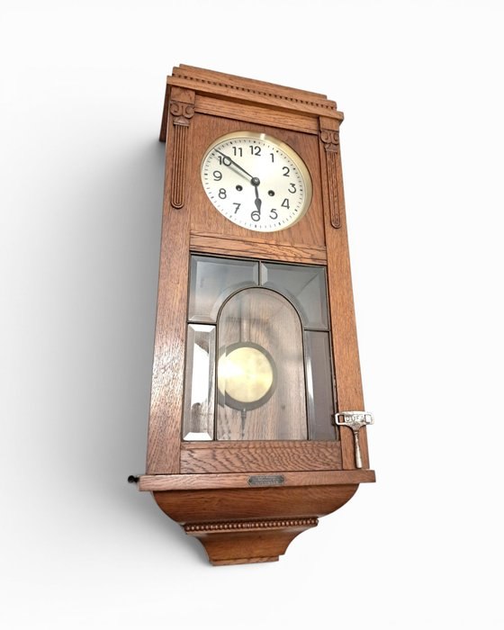 Oblique front view of the wooden box regulator wall clock with dial, pendulum, and key