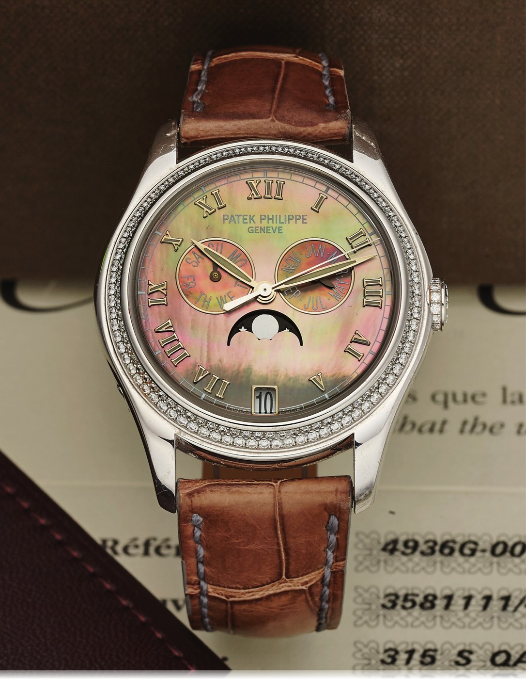 Front view of the Patek Philippe Ref. 4936G showing the diamond-set bezel, mother-of-pearl dial, and brown leather strap.
