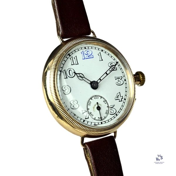 Oblique front view of the gold trench watch showing the white dial, blue 12 numeral, reeded bezel, and articulated lugs