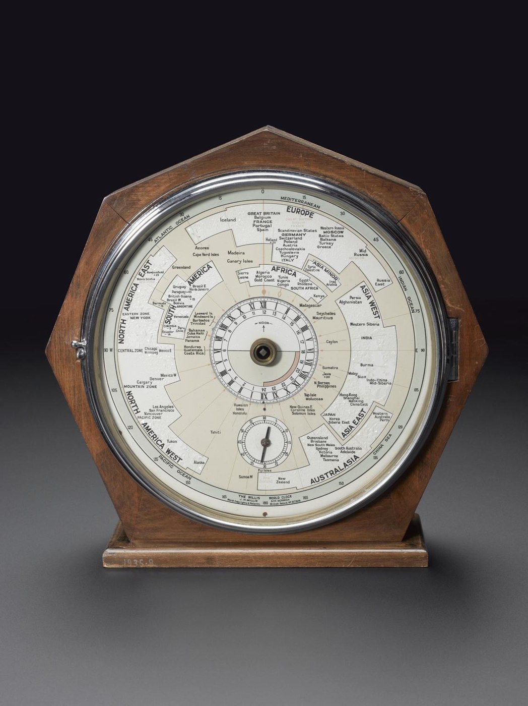 Front view of the Willis world clock showing the dial with geographical time zones, the minute subsidiary dial, and the hexagonal wooden case.