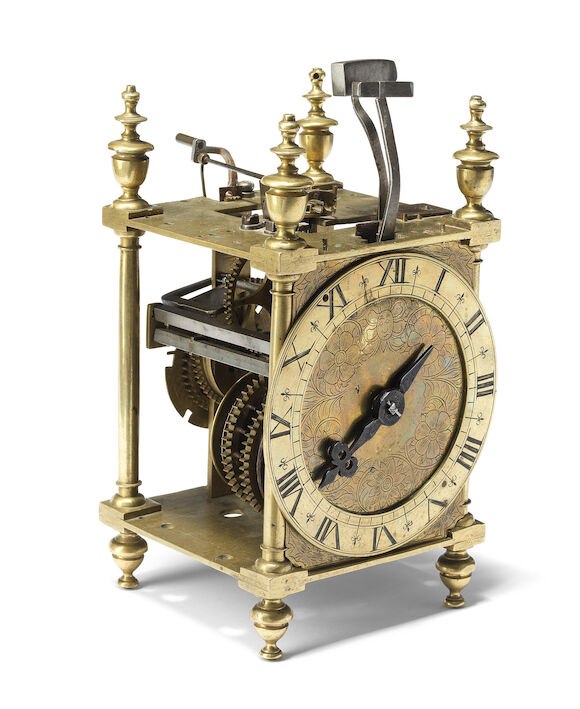 Three-quarter view of the unsigned brass lantern clock showing the dial, side movement frame, and top strike hammers