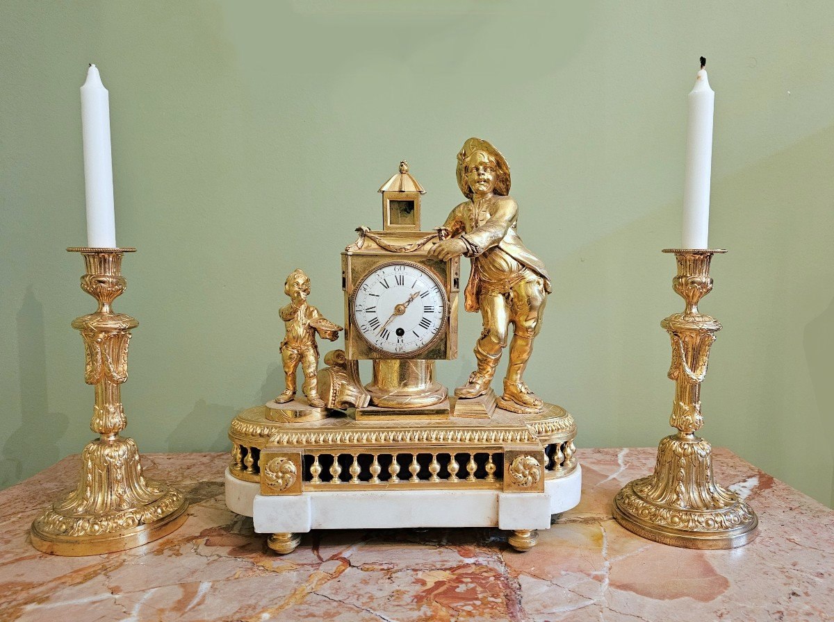 Frontal view of the gilt-bronze Louis XVI magic lantern mantel clock flanked by two decorative candlesticks
