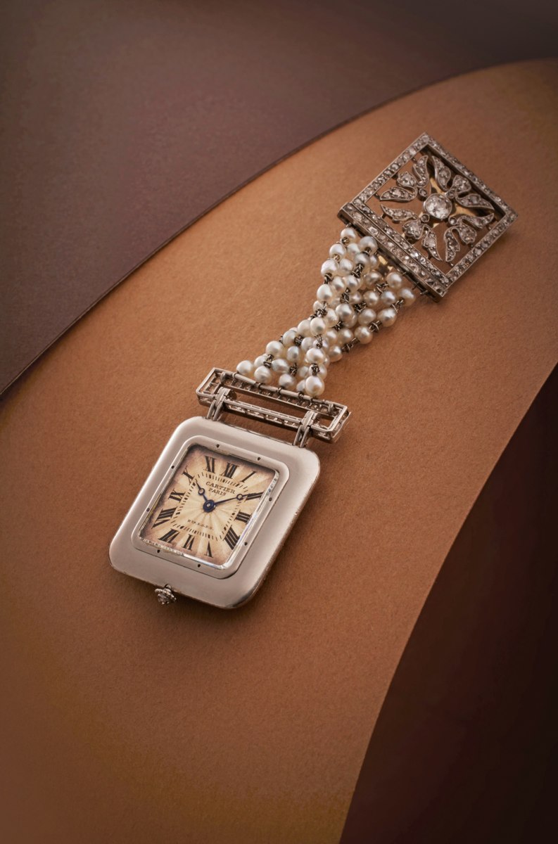 Obverse view of the cushion-form pendant watch attached to its pearl and diamond-set chatelaine