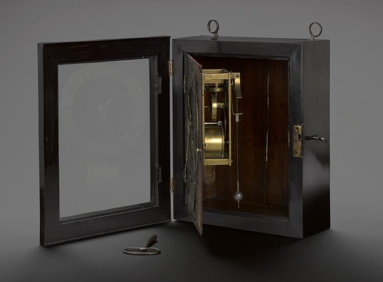 Three-quarter view of the Salomon Coster pendulum clock with open door revealing the movement, pendulum bob, and detached winding key