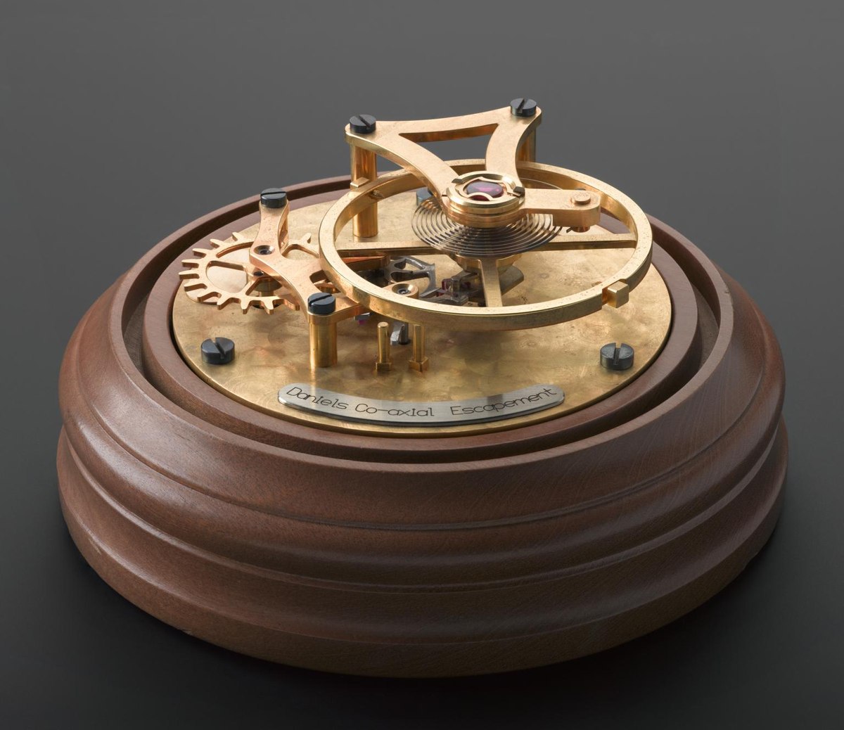 Demonstration model of the Daniels co-axial escapement made by Omega, mounted on a circular wooden plinth