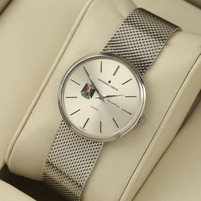 Front three-quarter view of the Universal Genève wristwatch on a display cushion, showing the dial with Iraqi emblem and mesh bracelet.