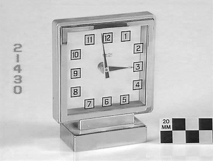 Side view of the Smiths English Clocks mystery clock showing the metal base, glass frame, and numerals on the inner glass surface.