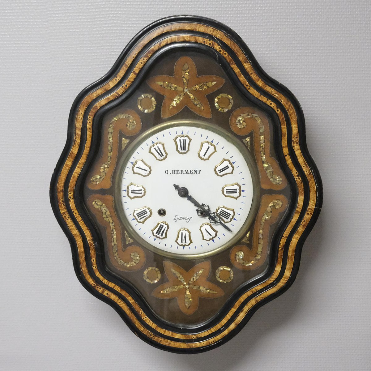 Front view of the G. Herment wall clock with mother-of-pearl inlay and shaped frame