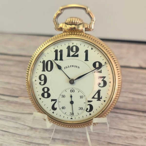 Front view of the open-face pocket watch showing the white dial, blued hands, and textured gold-filled bezel