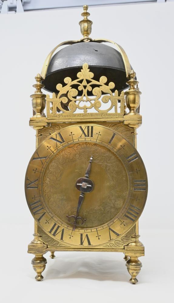 Front view of the John Pennocke lantern clock showing the pierced fret, floral engraved dial, chapter ring, and bell superstructure