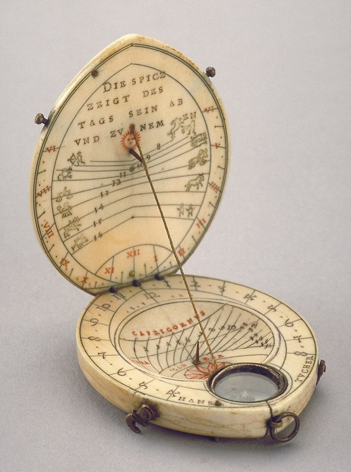 An open oval ivory and brass diptych dial showing the string gnomon, zodiacal markings, compass, and brass clasps.