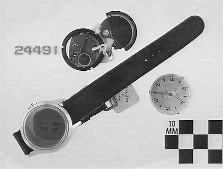 Disassembled components of the Timex wrist watch showing the casing with strap, the movement mechanism, and the dial face.