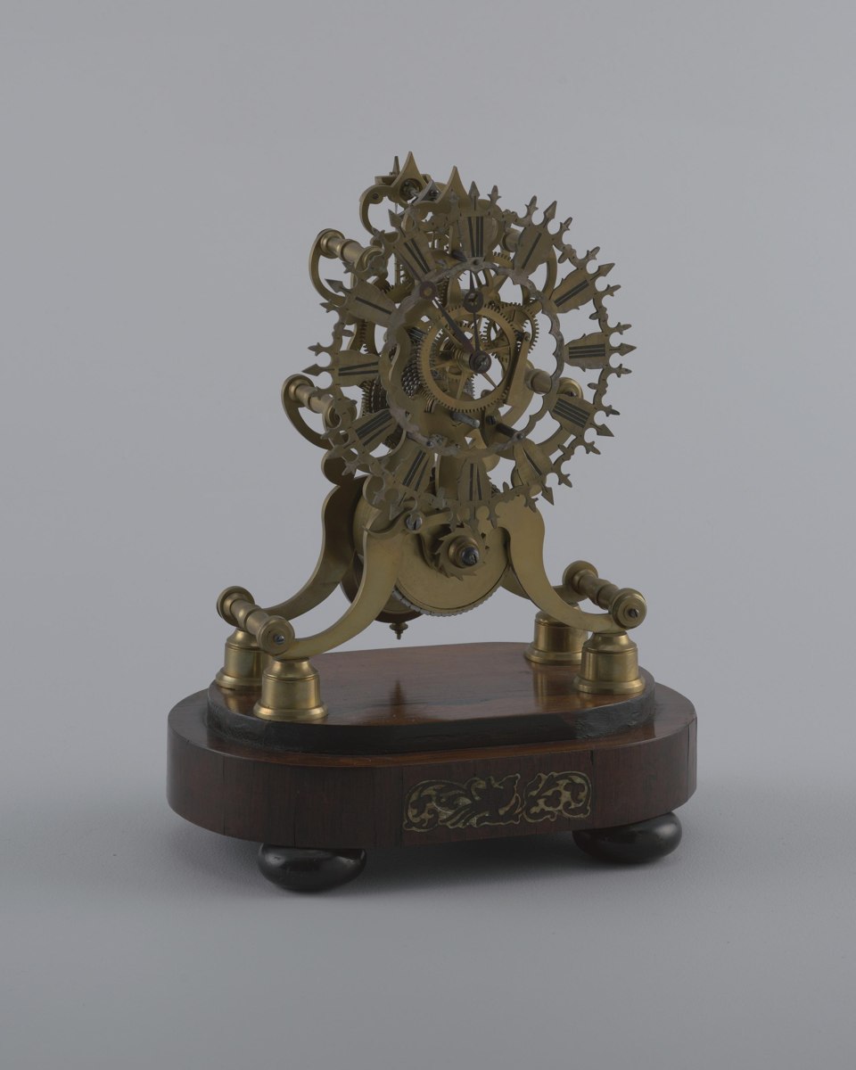 Three-quarter front view of the brass skeleton clock mounted on its wooden base