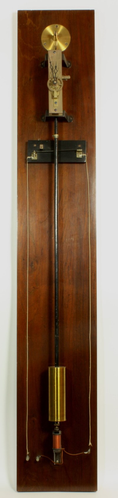 The impulse clock mounted on its vertical wooden backboard, showing the upper movement, central pendulum rod, and the lower electromagnetic impulse assembly.