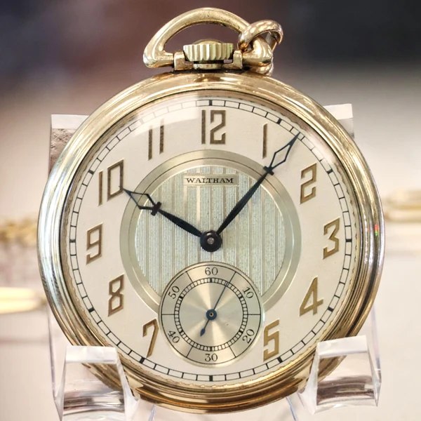 Dial and case front of the Waltham openface pocket watch resting on a clear stand