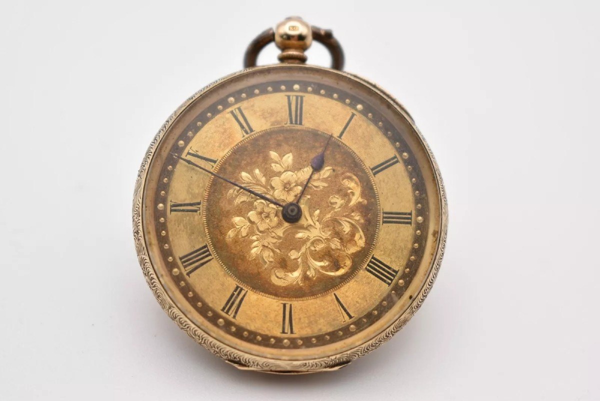Front view of the open-faced gold pocket watch showing the floral dial and Roman numerals