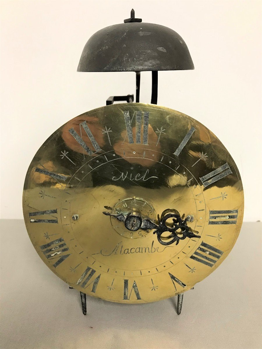 Front view of the 18th-century lantern clock signed Niel à Alacambe showing the circular dial, single hand, and bell