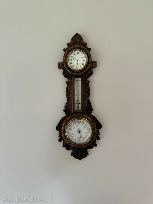 Front view of the Edwardian carved oak banjo clock barometer mounted against a wall