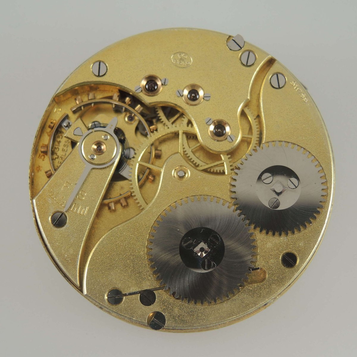 Top-plate view of the gilt IWC Peerless bridge movement showing the balance assembly, winding wheels, and Swiss signature