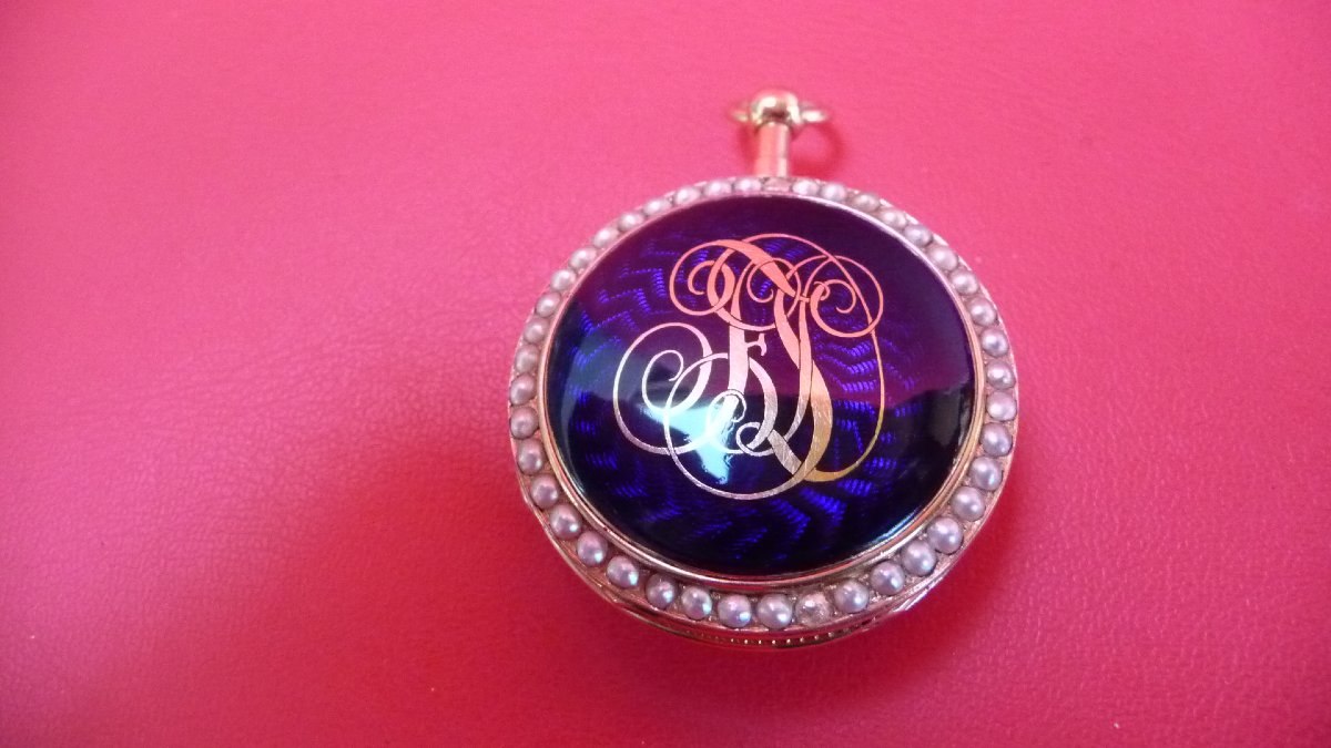 Reverse of the pocket watch showing the blue guilloché enamel caseback with gold monogram and pearl-set bezel