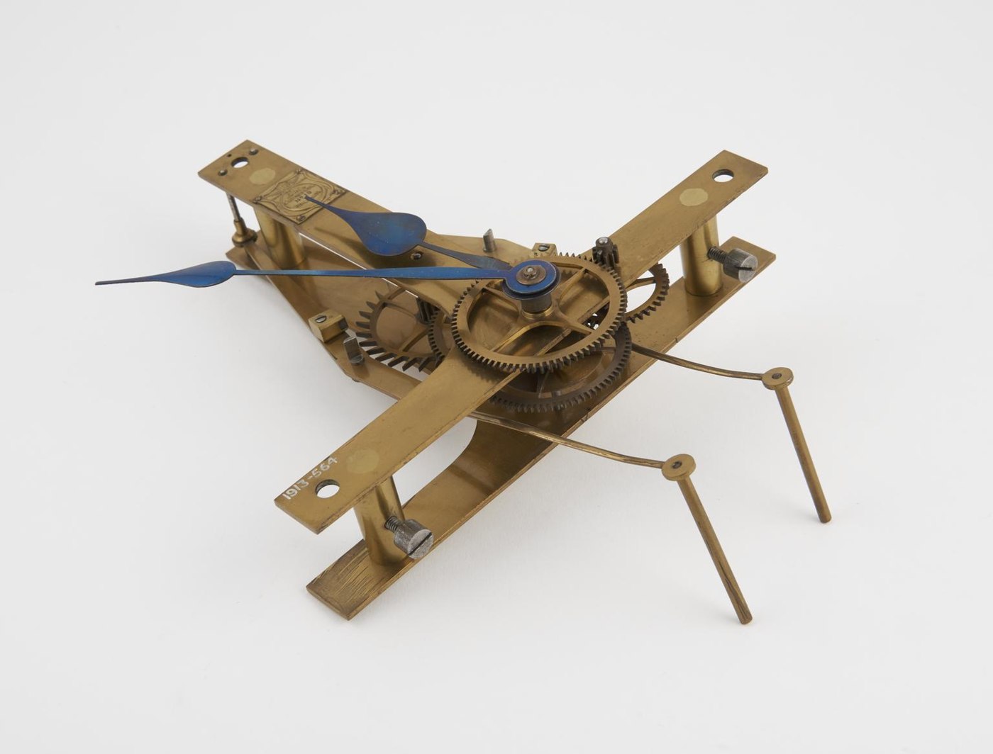 An electric slave clock mechanism with exposed brass movement and blue steel hands, bearing the accession number 1913-564.