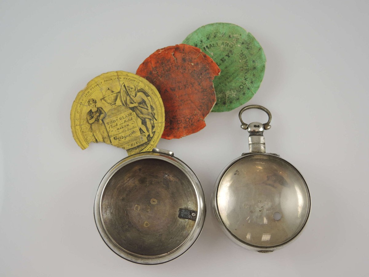 English silver inner and outer verge watch cases displayed with three watch papers and bullseye crystal