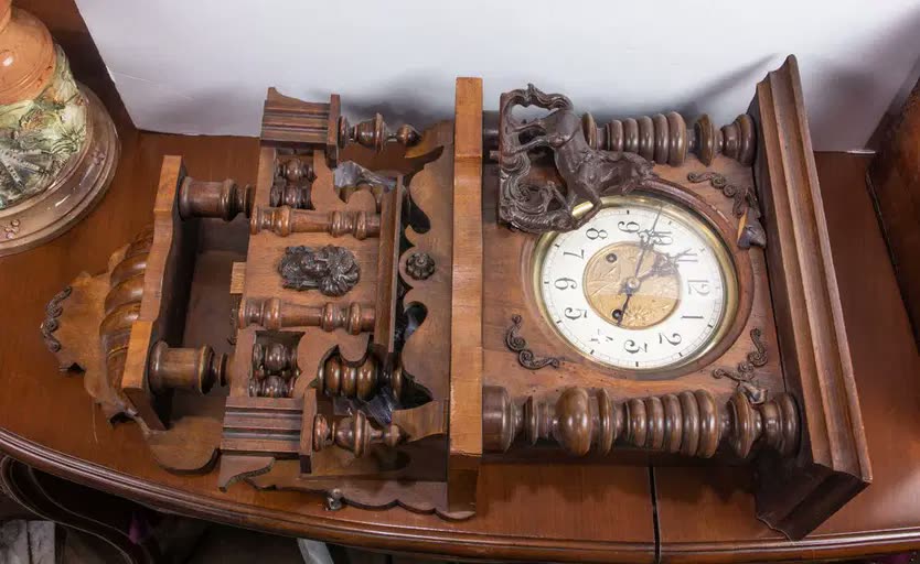 Front oblique view of the carved wooden wall clock case showing dial, horse crest, and turned woodwork