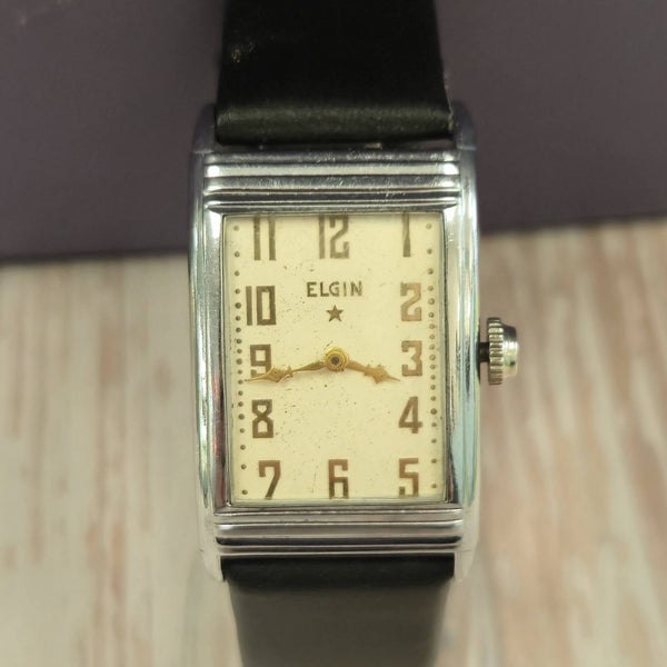 Front view of the rectangular Elgin wristwatch showing cream dial, Arabic numerals, and black strap
