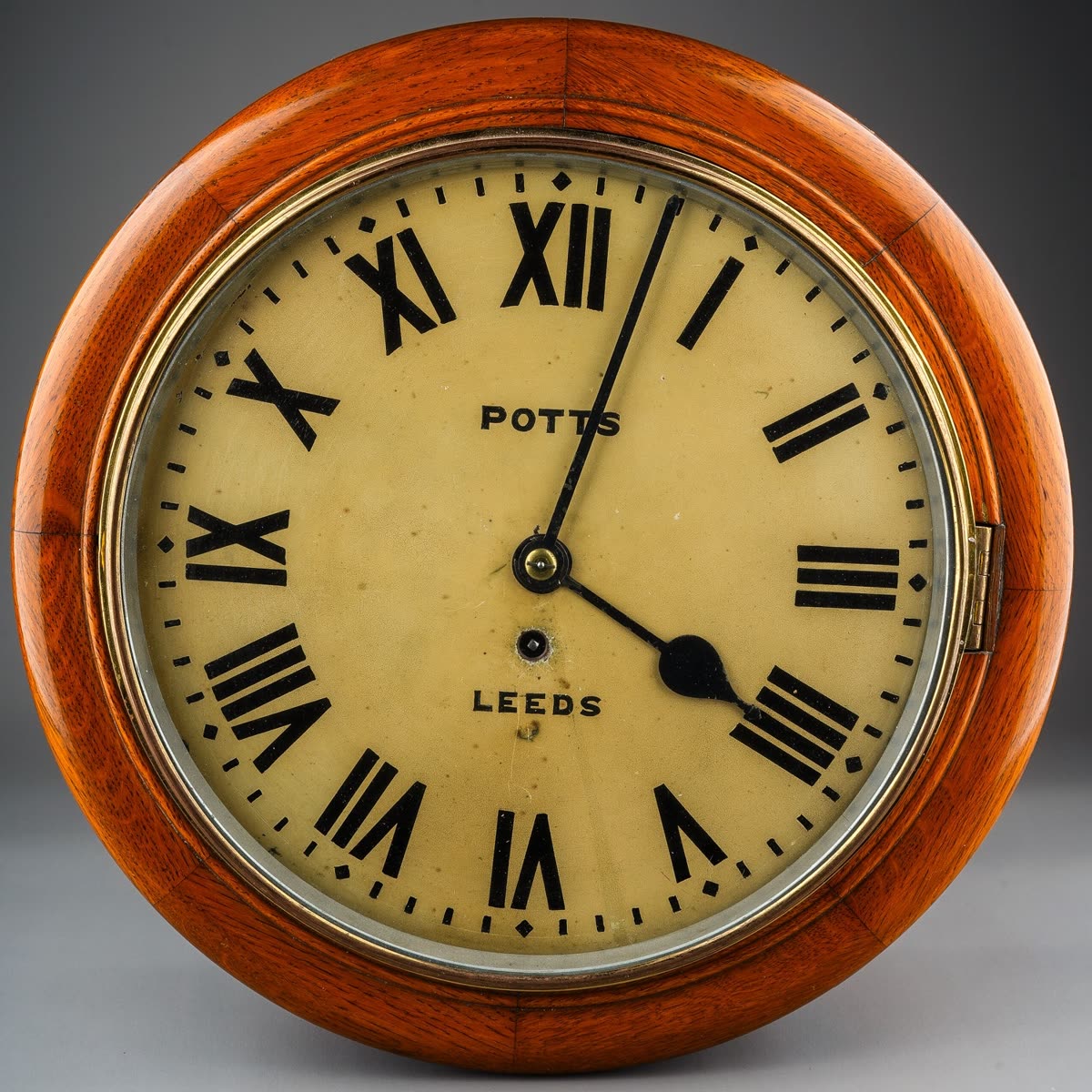 Front view of the Potts of Leeds wall clock showing the dial, hands, glazed brass bezel, and segmented mahogany case surround