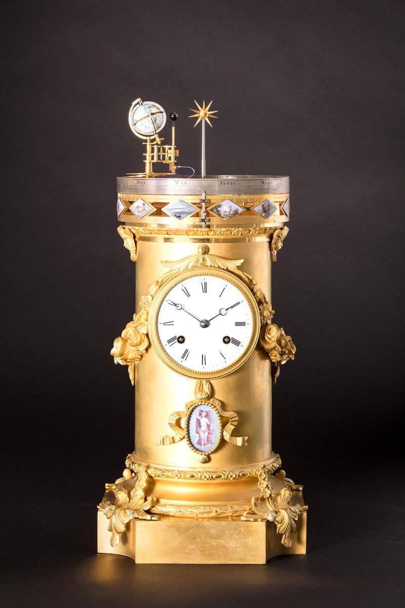 The cylindrical gilded bronze case, decorated with garlands of roses, leaves and ribbons, stands on a square base with concave corners (MIH IV-135)