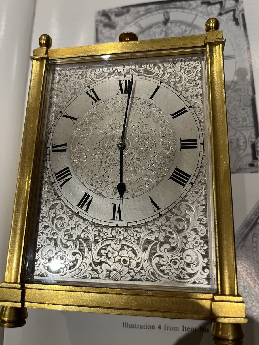 Front view of the gilt-brass clock showing the engraved floral dial, Roman numeral chapter ring, and case finials