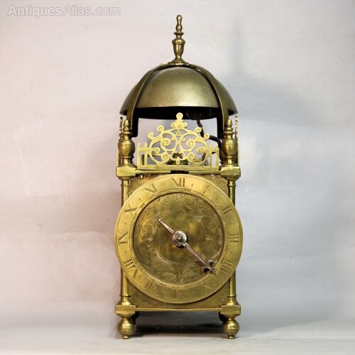 Front view of the English lantern clock showing the engraved dial, single hand, pierced fret, and bell assembly