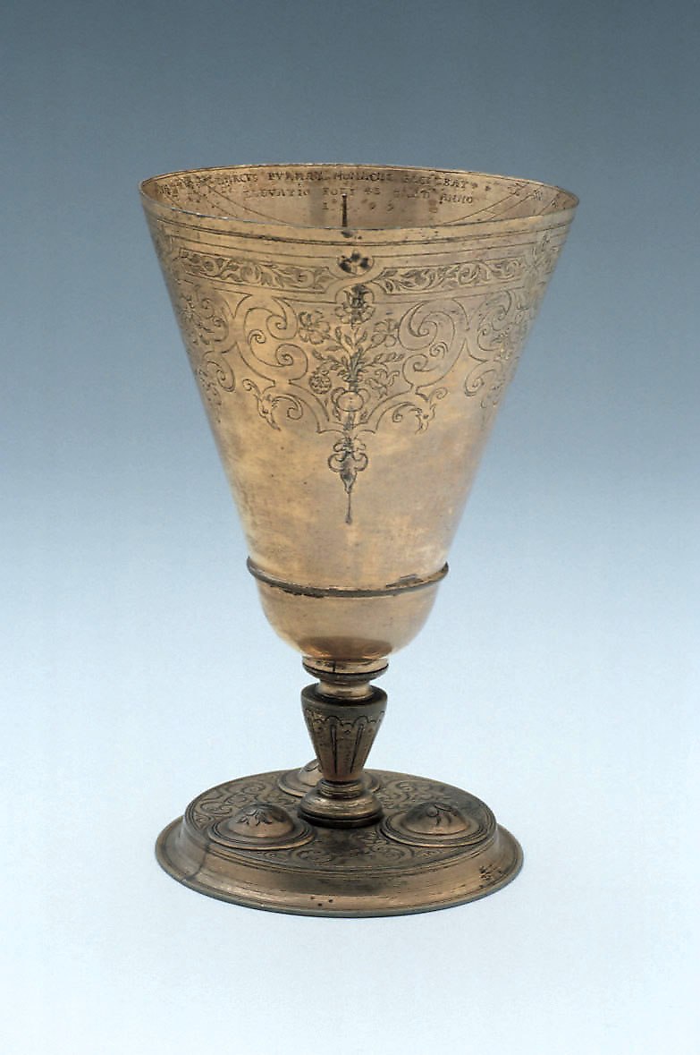 A gilt brass chalice dial with floral engravings, a central gnomon, and a base with three bosses.