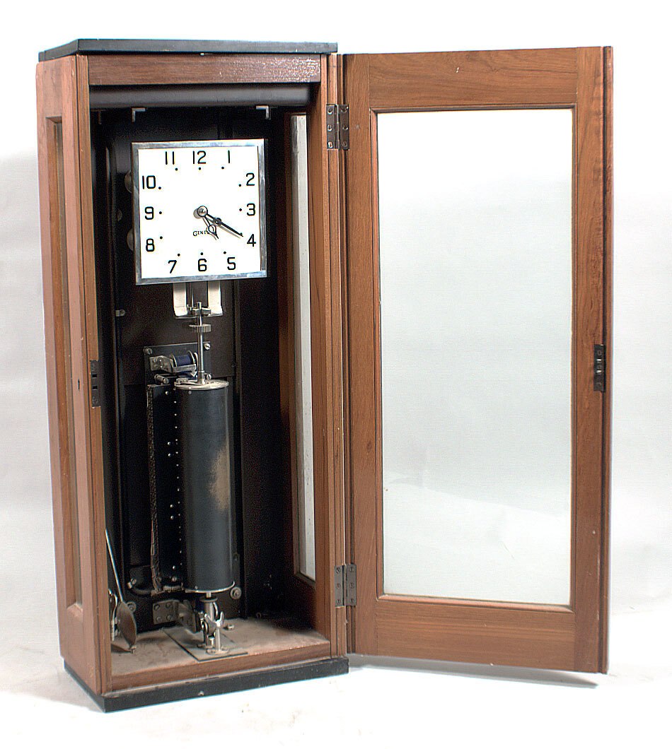 A front view of the Gents' of Leicester time clock, showing the wooden cabinet with a glass door, the square dial, the pendulum, and the recording cylinder.