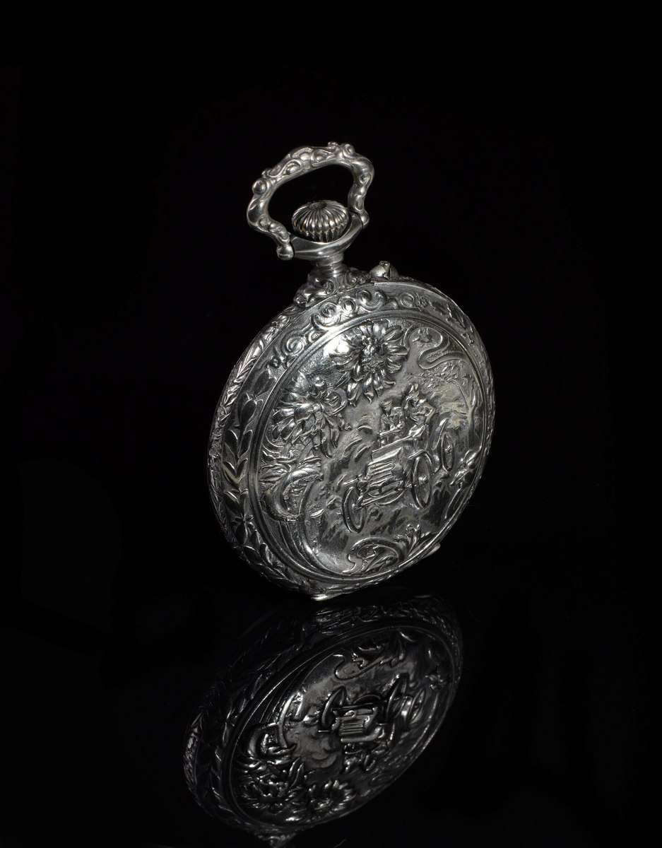 Three-quarter rear view of the embossed touring pocket watch case against a reflective dark surface