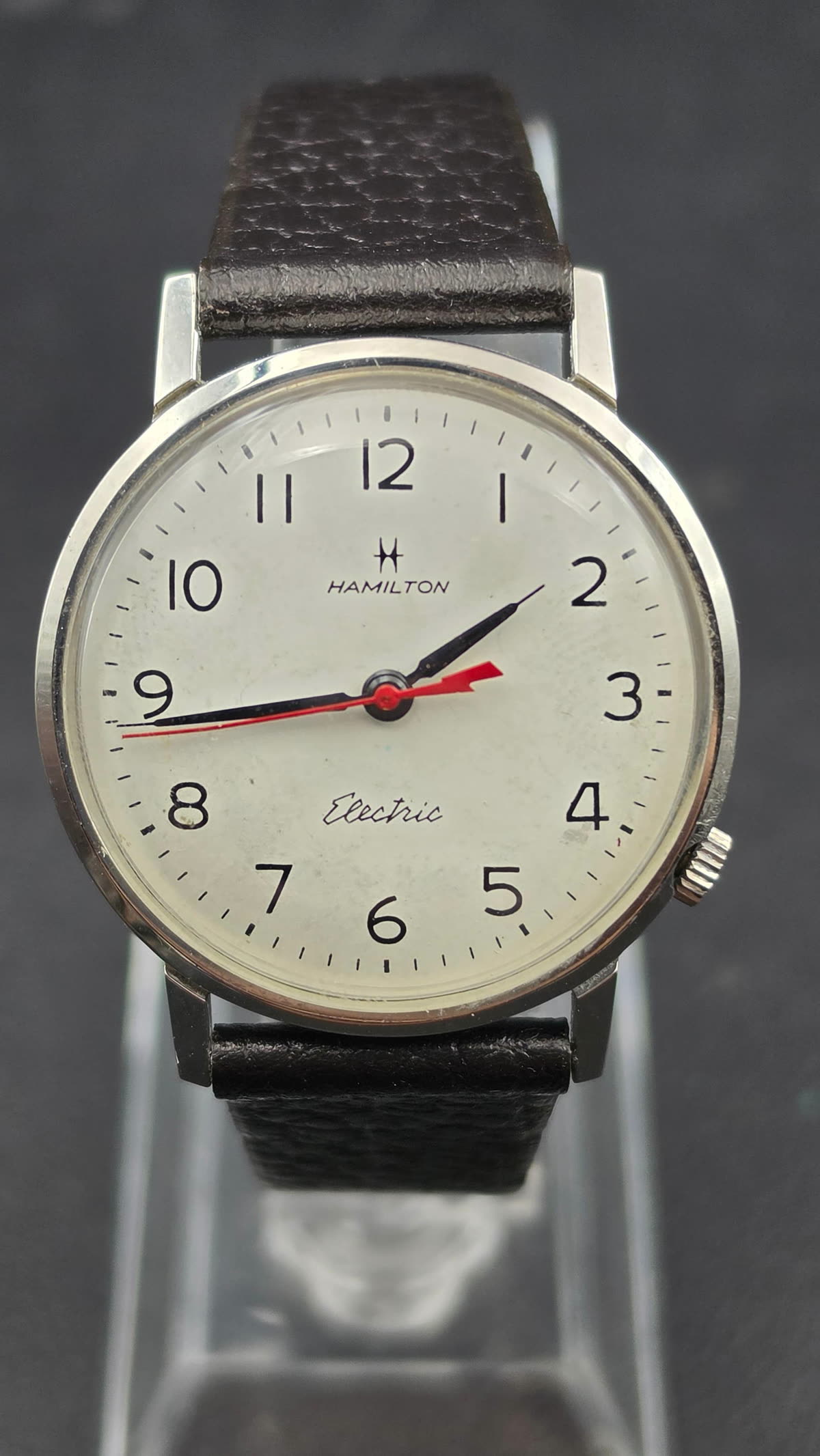 Front view of the Hamilton Electric wristwatch showing dial, hands, and case on display stand