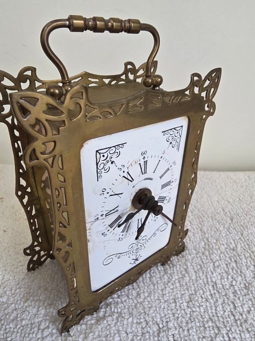 Three-quarter view of the brass bracket clock showing the dial, pierced case, and handle