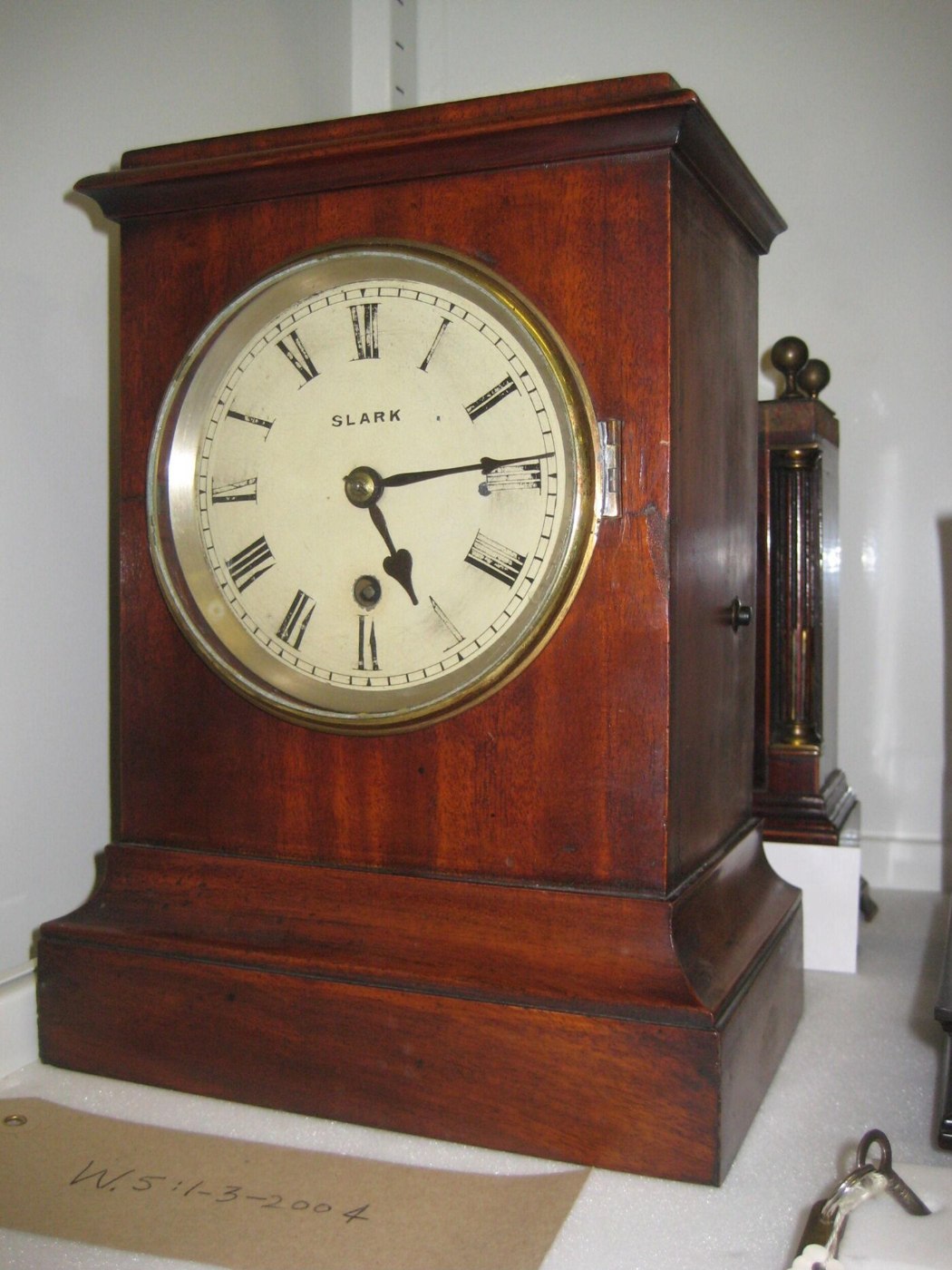 Front view of the Slark mahogany mantle clock showing the painted Roman numeral dial and the accession tag W.5:1-3-2004.