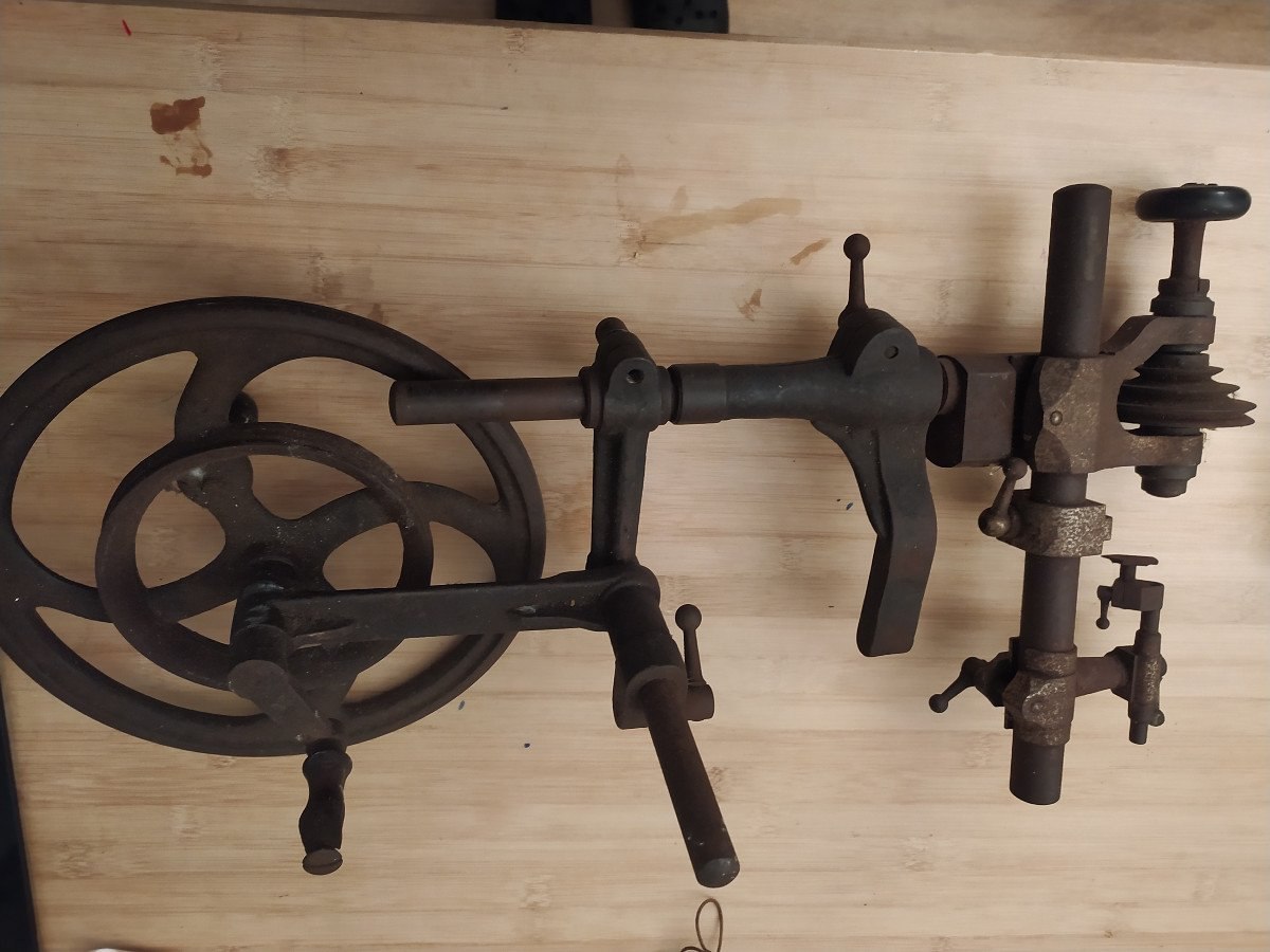 Full view of the metal watchmaker's lathe showing the spoked drive wheel, support arm, and stepped pulley assembly