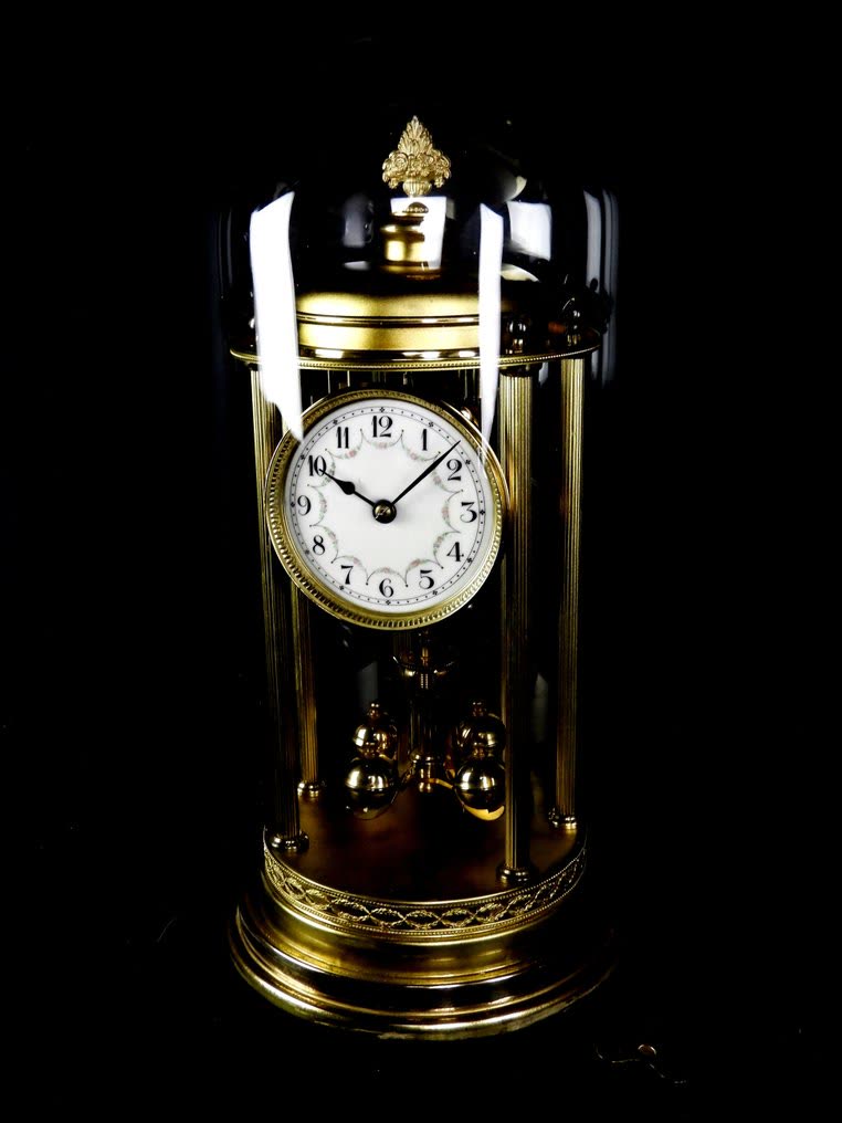 Frontal view of the August Schatz & Söhne brass anniversary clock under a glass dome with rotary pendulum