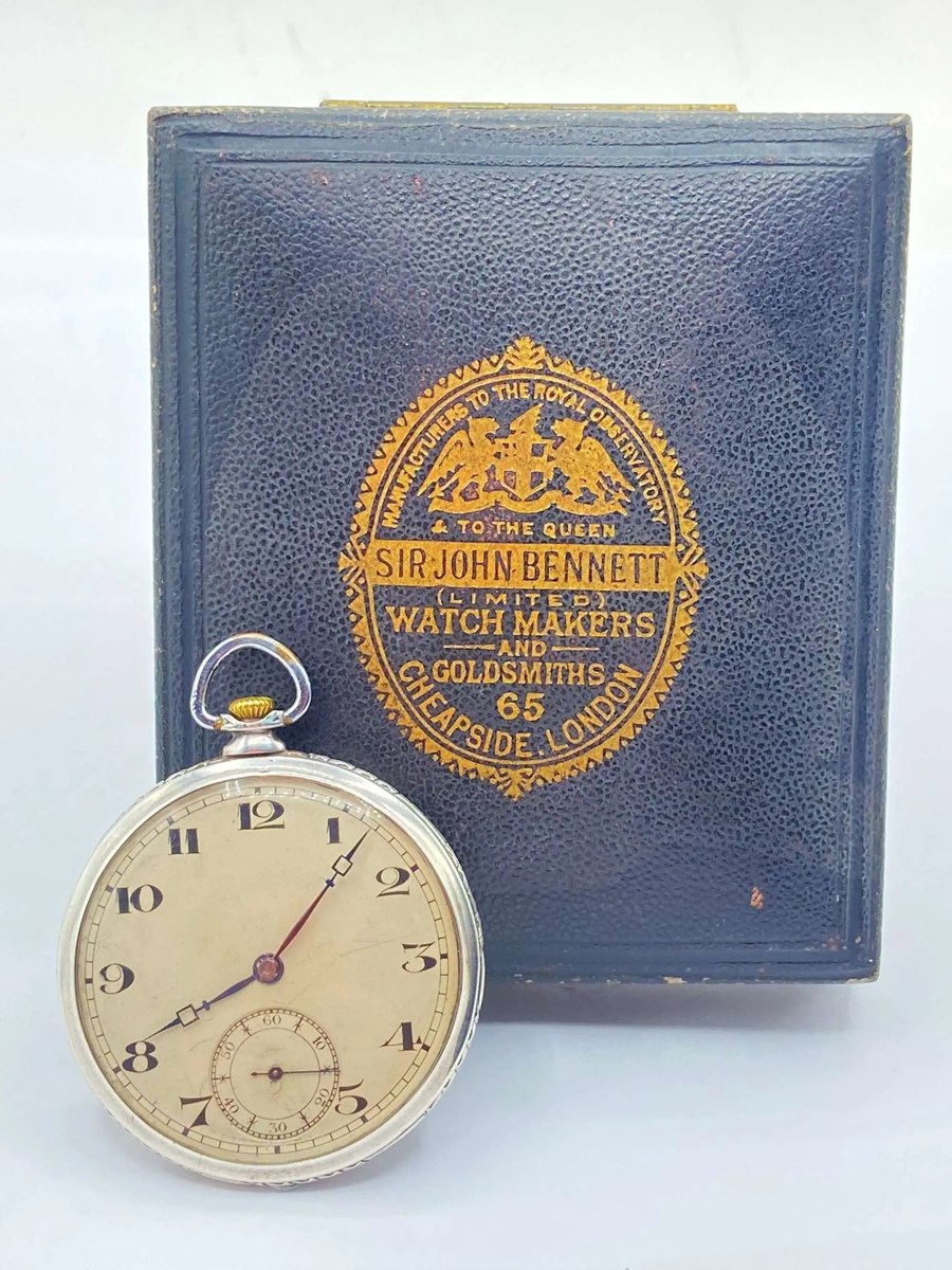 Dial view of the open-face pocket watch set in front of its gilt-stamped leather box
