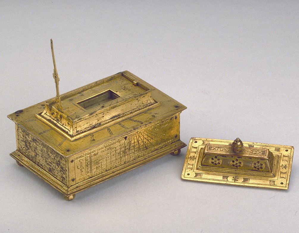 A horizontal dial casket of gilt copper with a hinged lid, featuring a compass, string gnomon dial, and various astronomical tables.