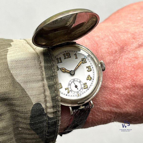 Wristlet watch in a silver hunter case with hinged cover open, displaying a white enamel dial with sub-seconds register