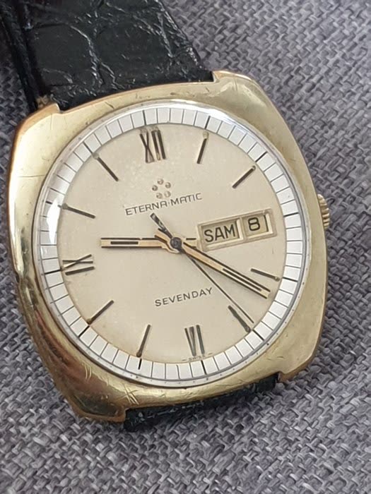 Front view of the cushion-shaped gold-tone Eterna-Matic Sevenday wristwatch on a dark textured strap